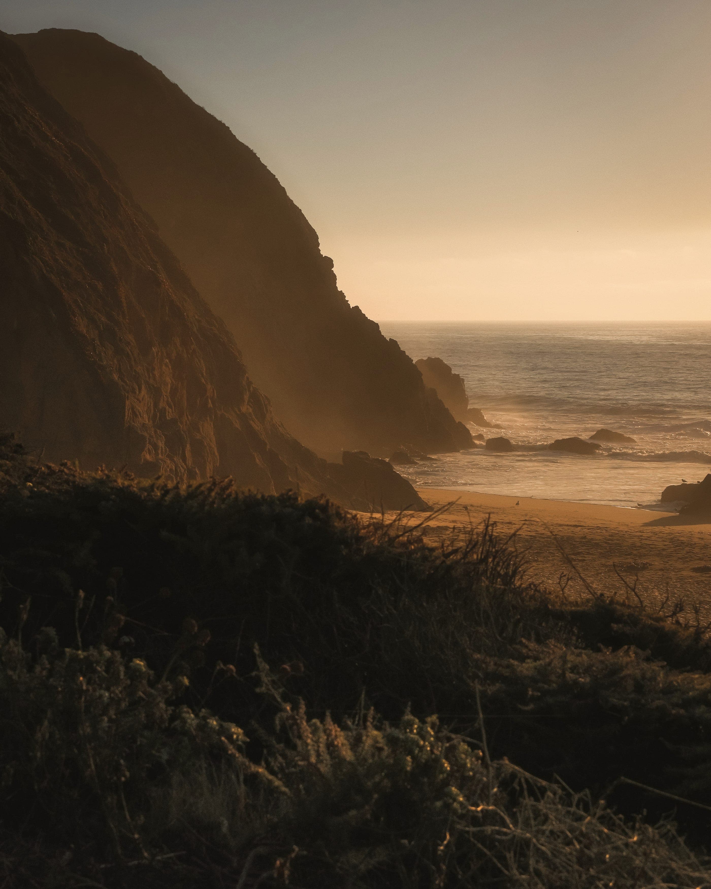 A headland above a beach at low sun, the sea going pale to the horizon.