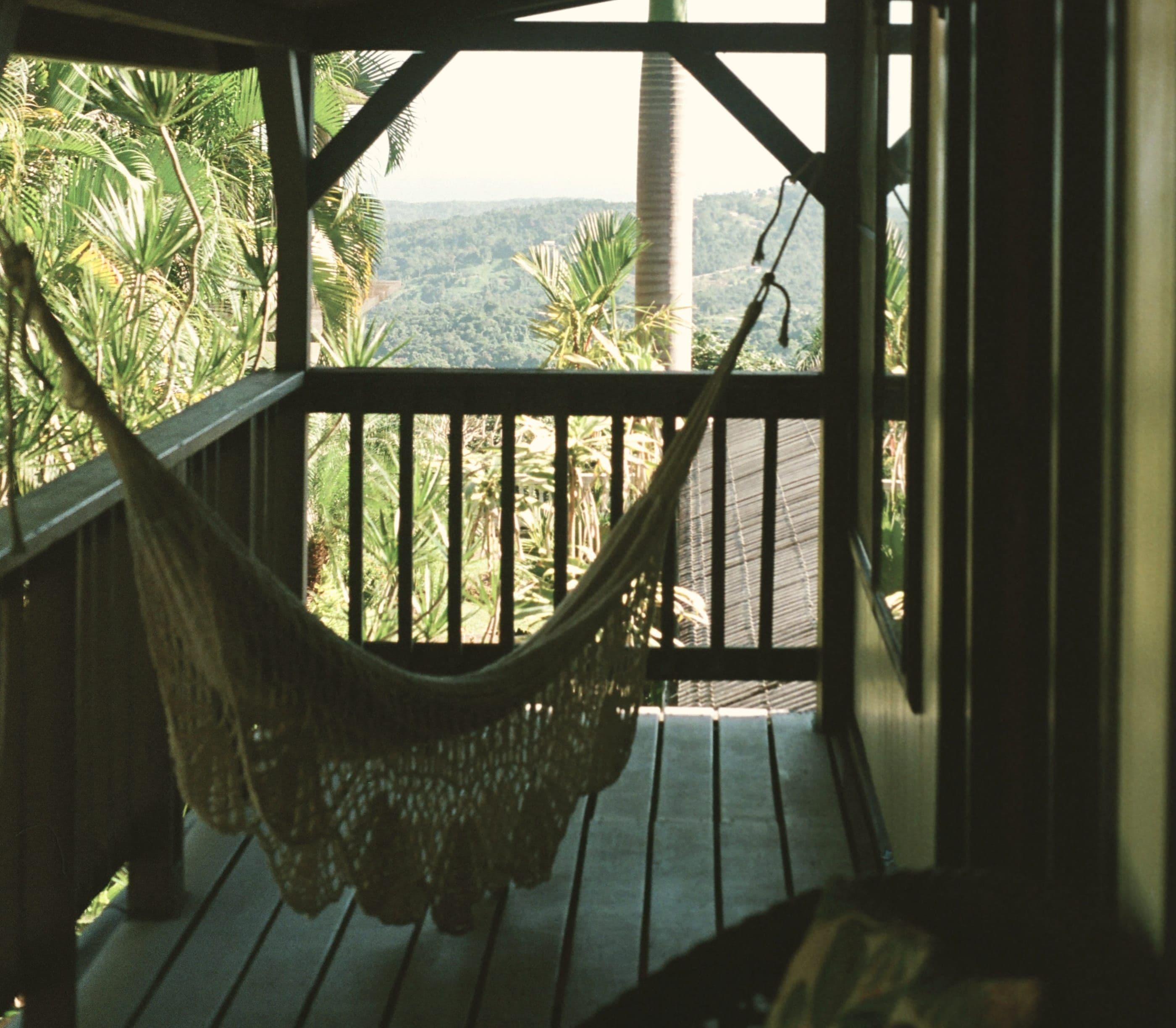 A hammock on a dark timber porch, lanterns lit against the trees.